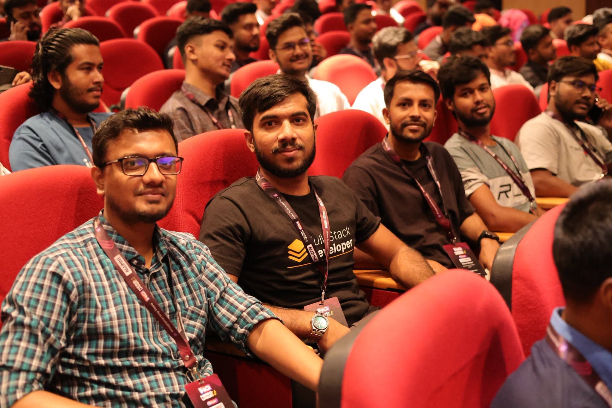 Mamun Ahmed seated with other alumni in red auditorium seats at Hero Union 2.0, attendees wearing event lanyards and Full-Stack Developer shirts.