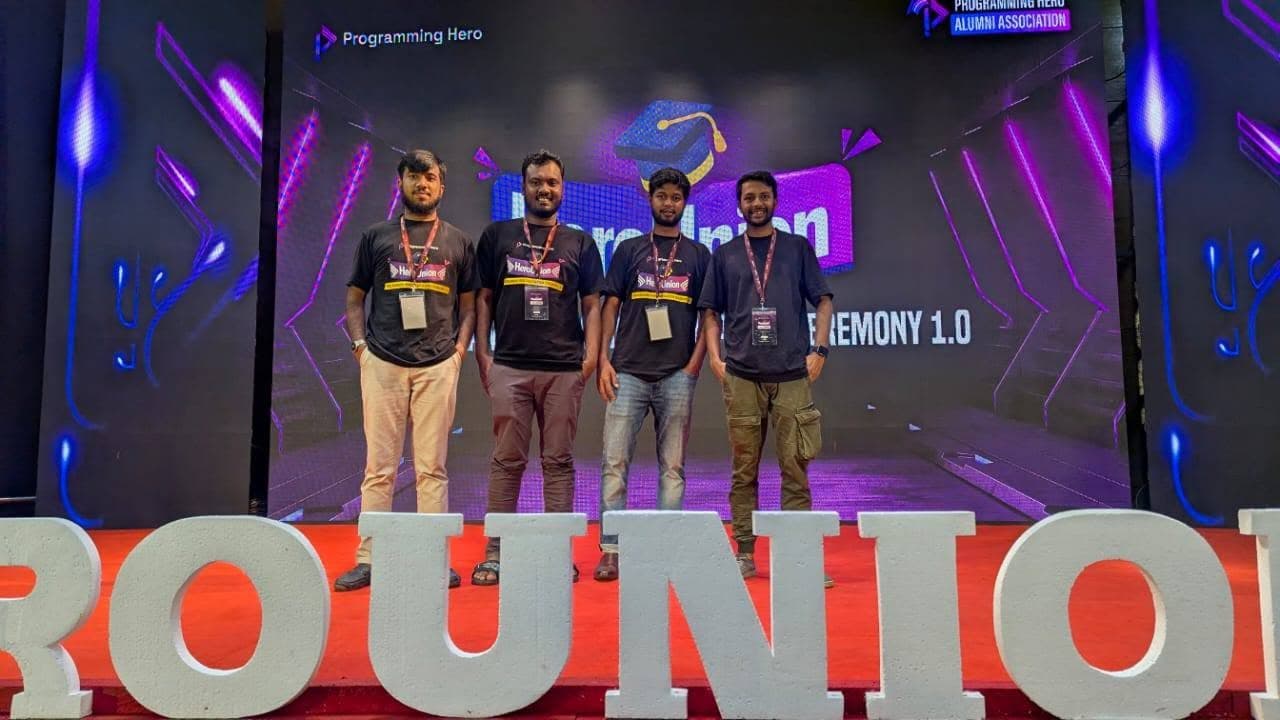 Four attendees in HeroUnion shirts standing on the HeroUnion 1.0 ceremony stage in front of a purple LED backdrop.